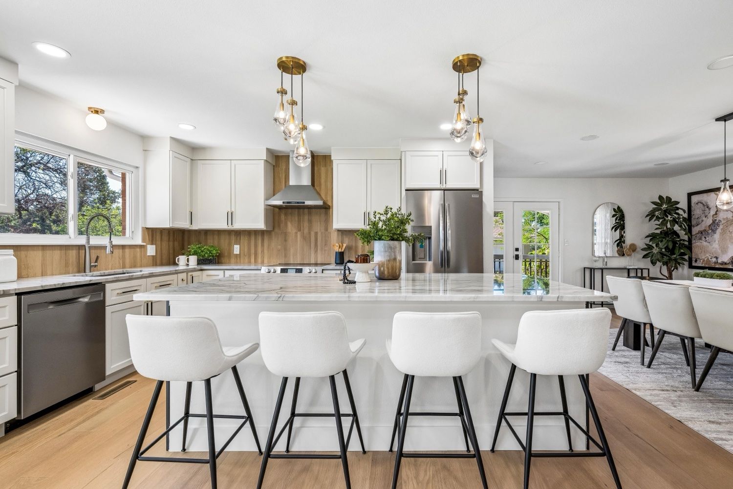 Open-concept kitchen with white shaker cabinets, quartzite island, wood-look backsplash and brass glass pendants